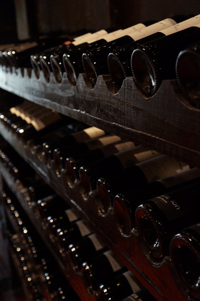 A dimly lit wine cellar showcasing rows of wine bottles on rustic wooden shelves, creating a classic and elegant atmosphere.